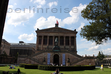 Nationalgalerie in Berlin auf der Museumsinsel wo Ausstellungen gezeigt werden. Auf dem Rasen vor der Nationalgalerie sitzen Touristen in der Sonne und ruhen sich aus.
